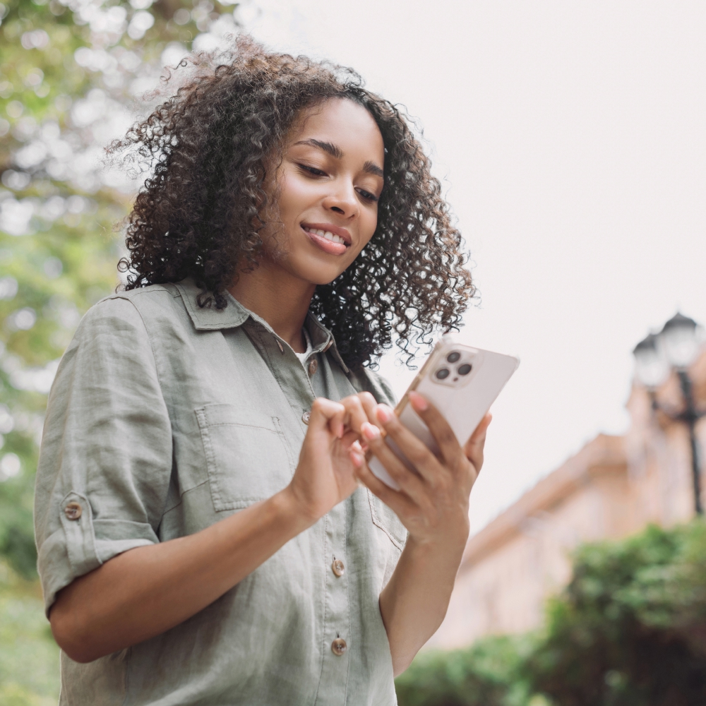 Smiling woman using smartphone outdoors in summer